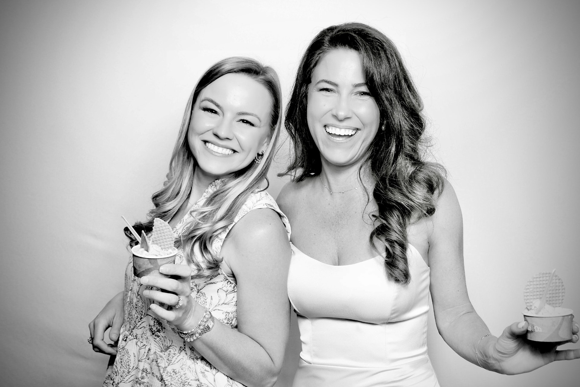 Two guests smiling with dessert in a black-and-white studio portrait