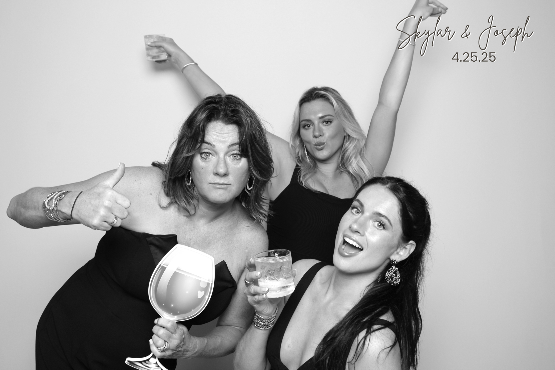 Three guests in dark formalwear make playful expressions with drinks and a novelty wine-glass prop.