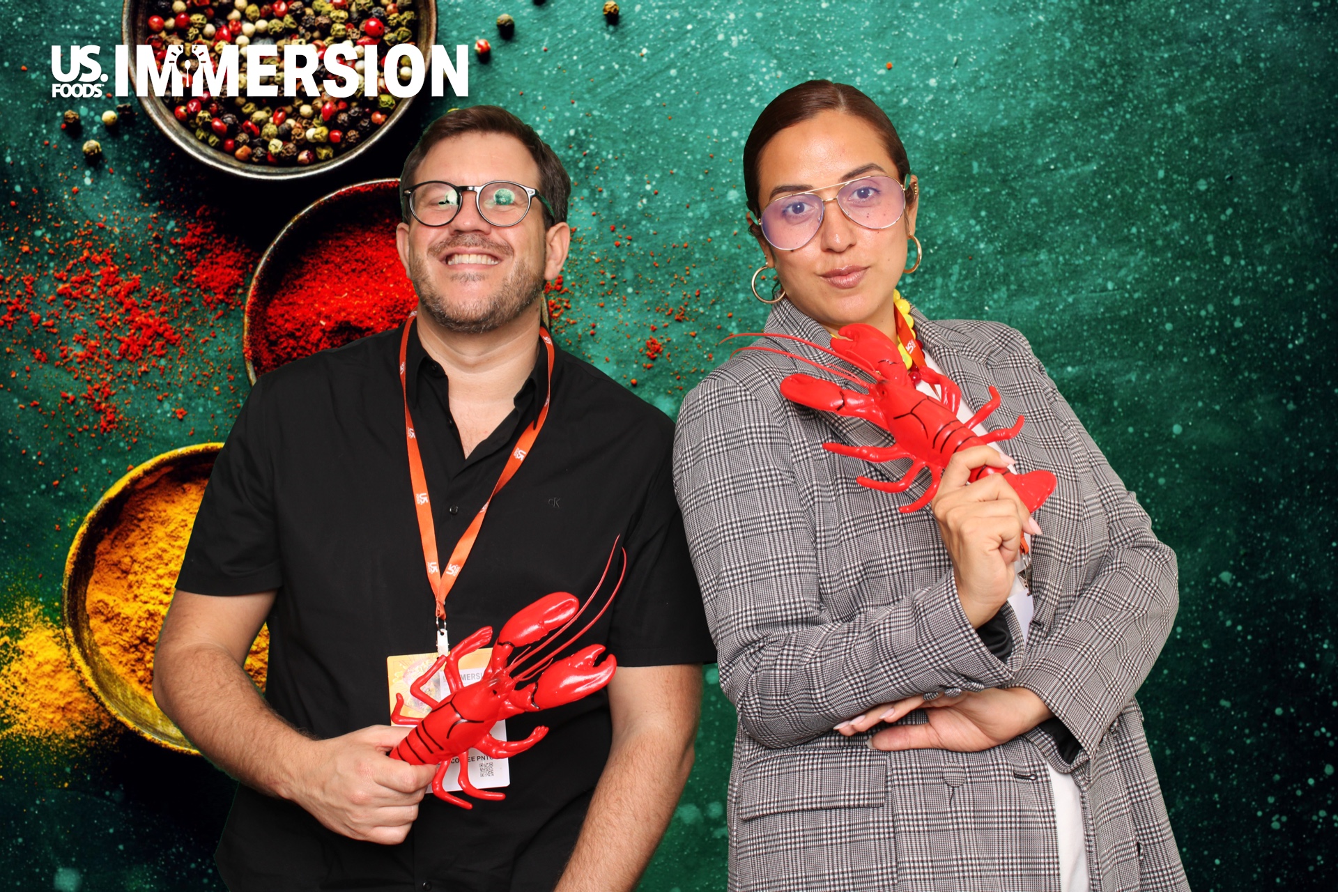 Two guests posing with lobster props on a spice green screen backdrop