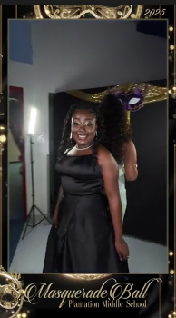 A student in a black gown posing beside a gold masquerade mask display