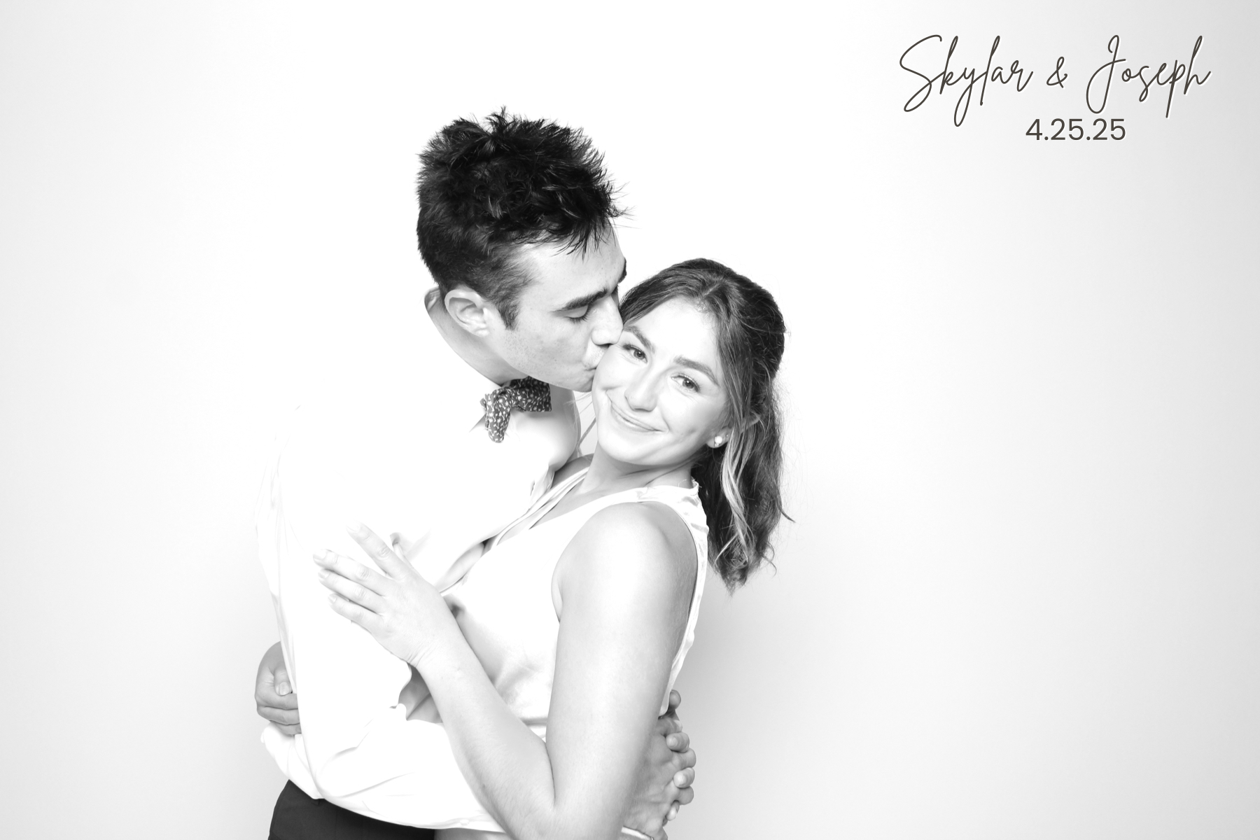 Two guests in formal attire embrace while one kisses the other on the cheek.