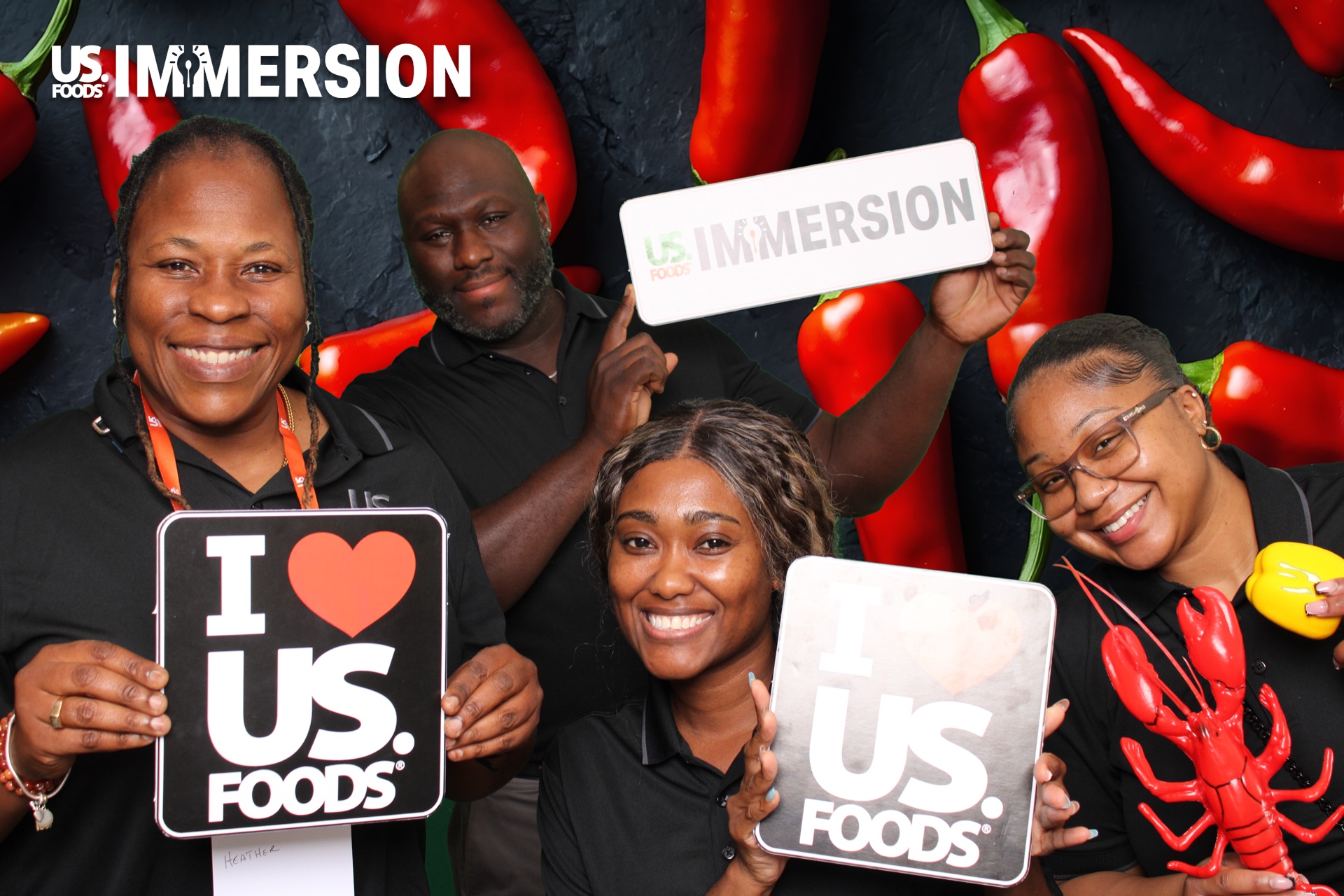 Four US Foods attendees laughing with branded signs on a chili pepper backdrop