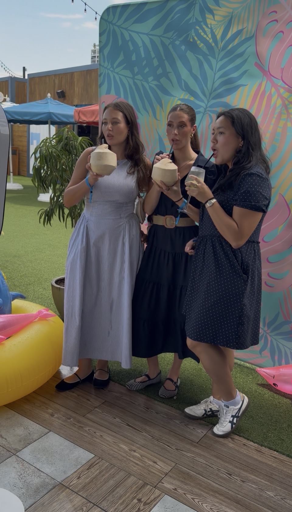 Three guests sipping coconuts in front of the tropical photo backdrop