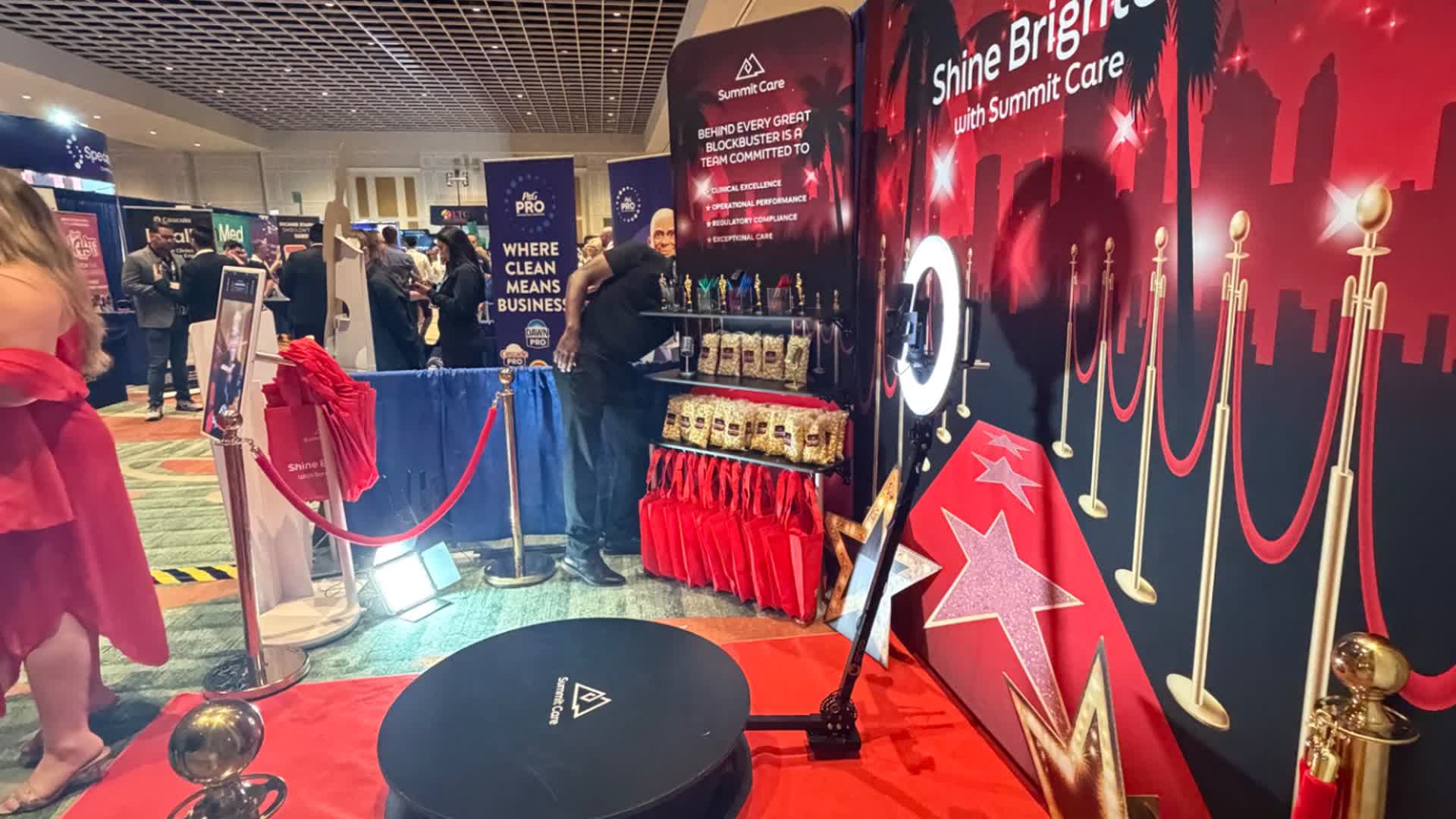 Wide view of the Summit Care exhibit with 360 platform, red carpet, stanchions, custom backdrop and prize display