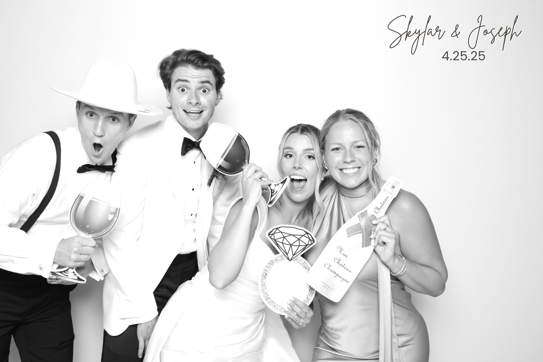 Four wedding guests in formal attire pose with celebratory props and a novelty wine-glass.