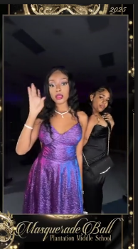 Two students in purple and black formal outfits posing together in the gold Masquerade Ball frame