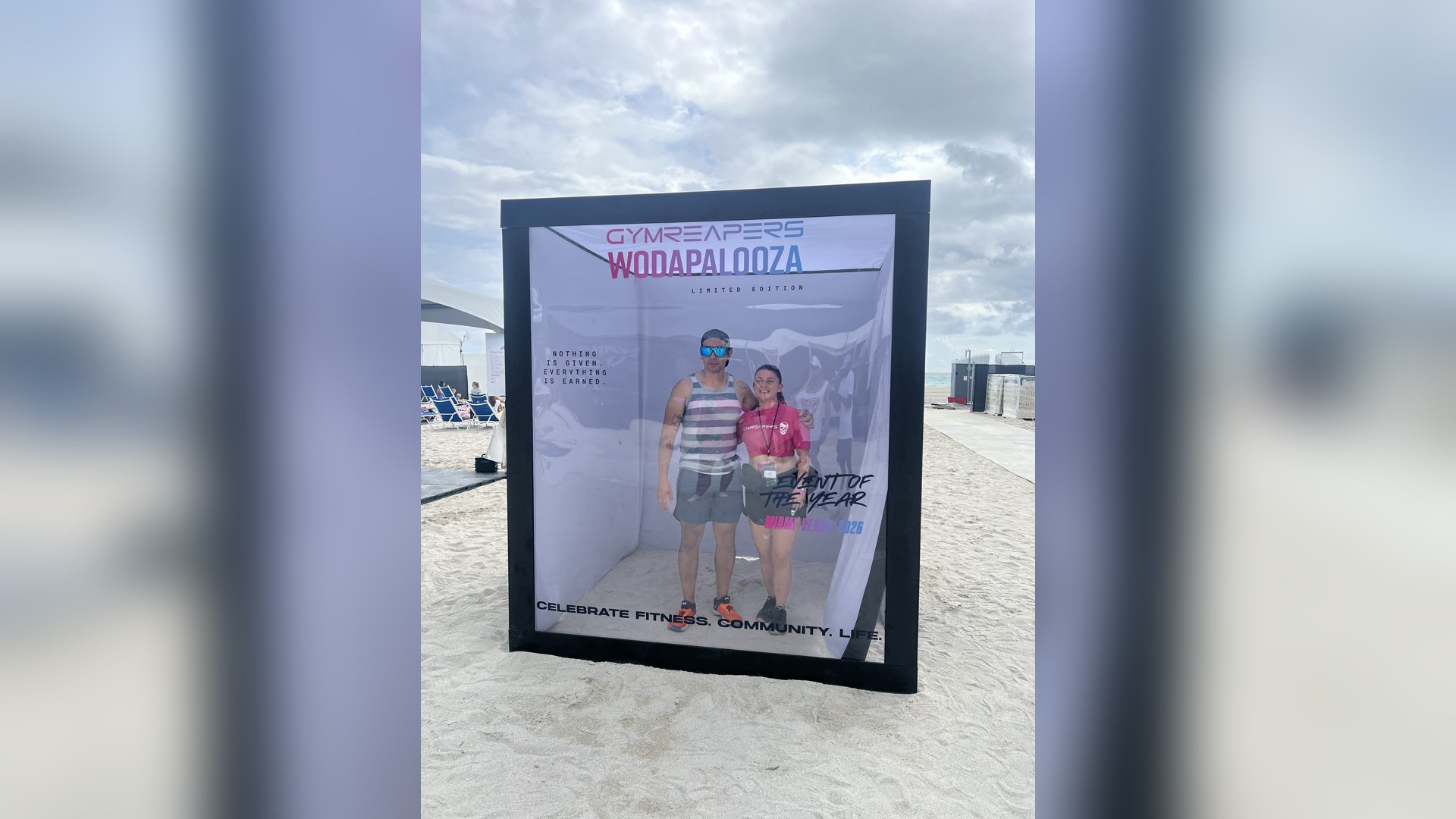 The life-size SnapJoy Magazine Cover Studio on the sand at Wodapalooza in Miami Beach, with two attendees posing inside the transparent Wodapalooza cover