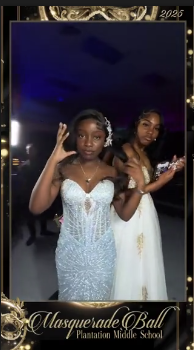 Two students in formal gowns posing together inside the gold Masquerade Ball frame