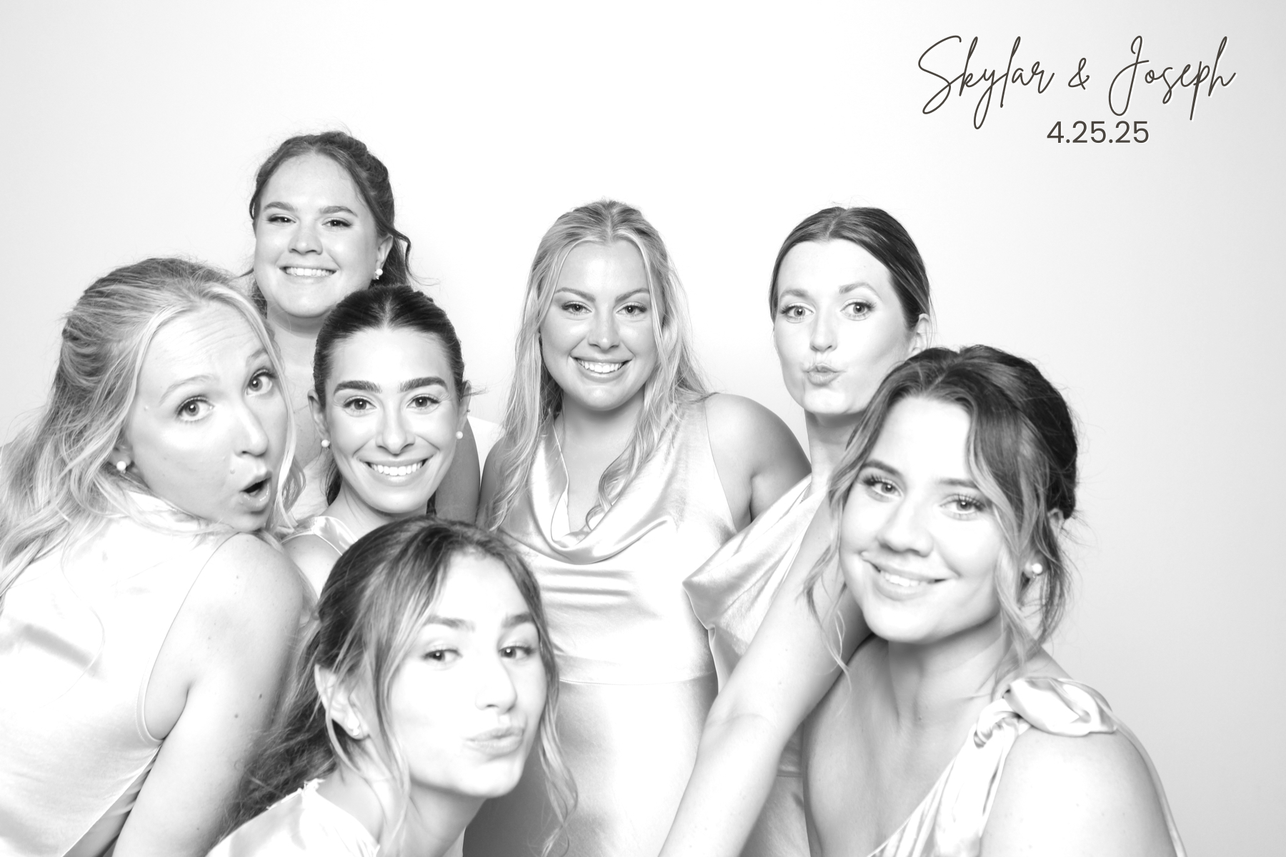 Group of women in satin dresses gathers closely for a playful black-and-white portrait.