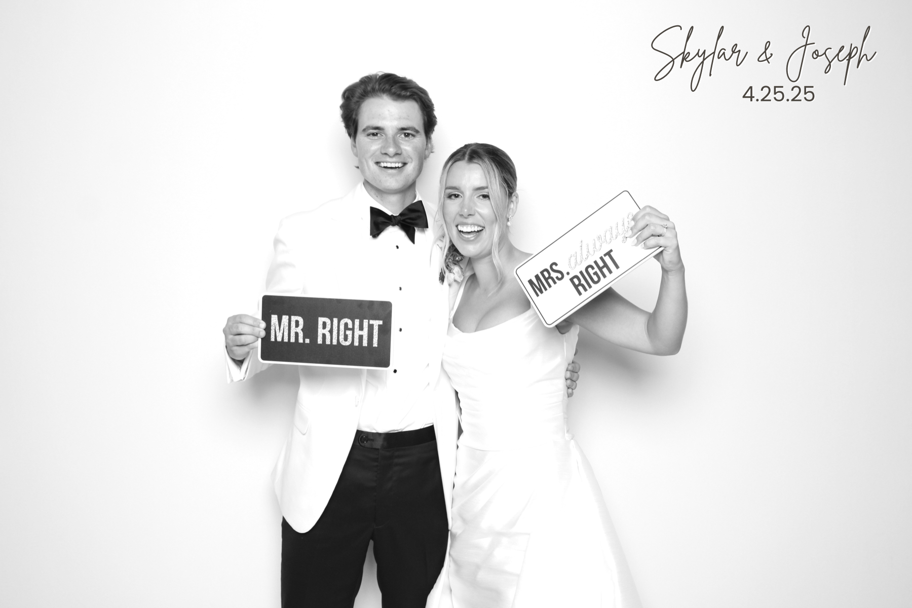 Couple in wedding attire holds playful wedding signs in a bright studio portrait.