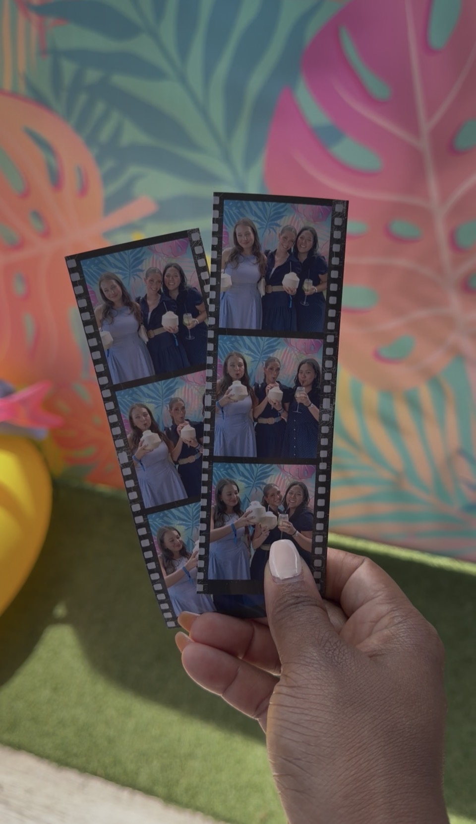 Two printed photo strips held up against the tropical backdrop
