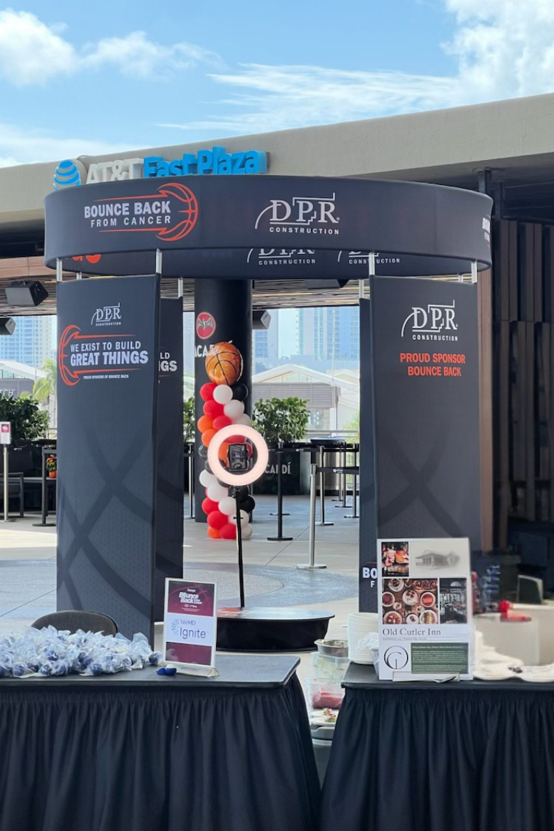Entrance of the enclosed 360 Pavilion showing Bounce Back From Cancer and DPR Construction banners with a basketball balloon column