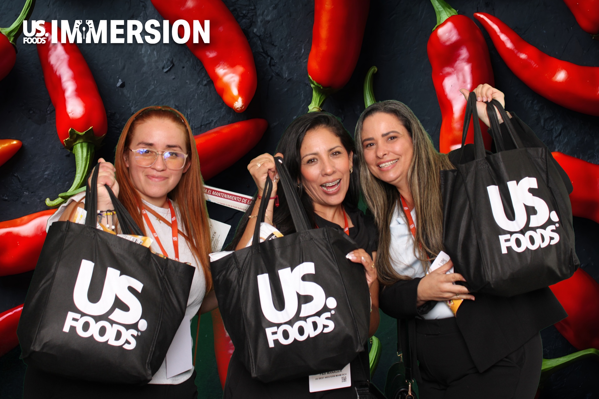 Three attendees holding US Foods tote bags in front of a chili pepper backdrop