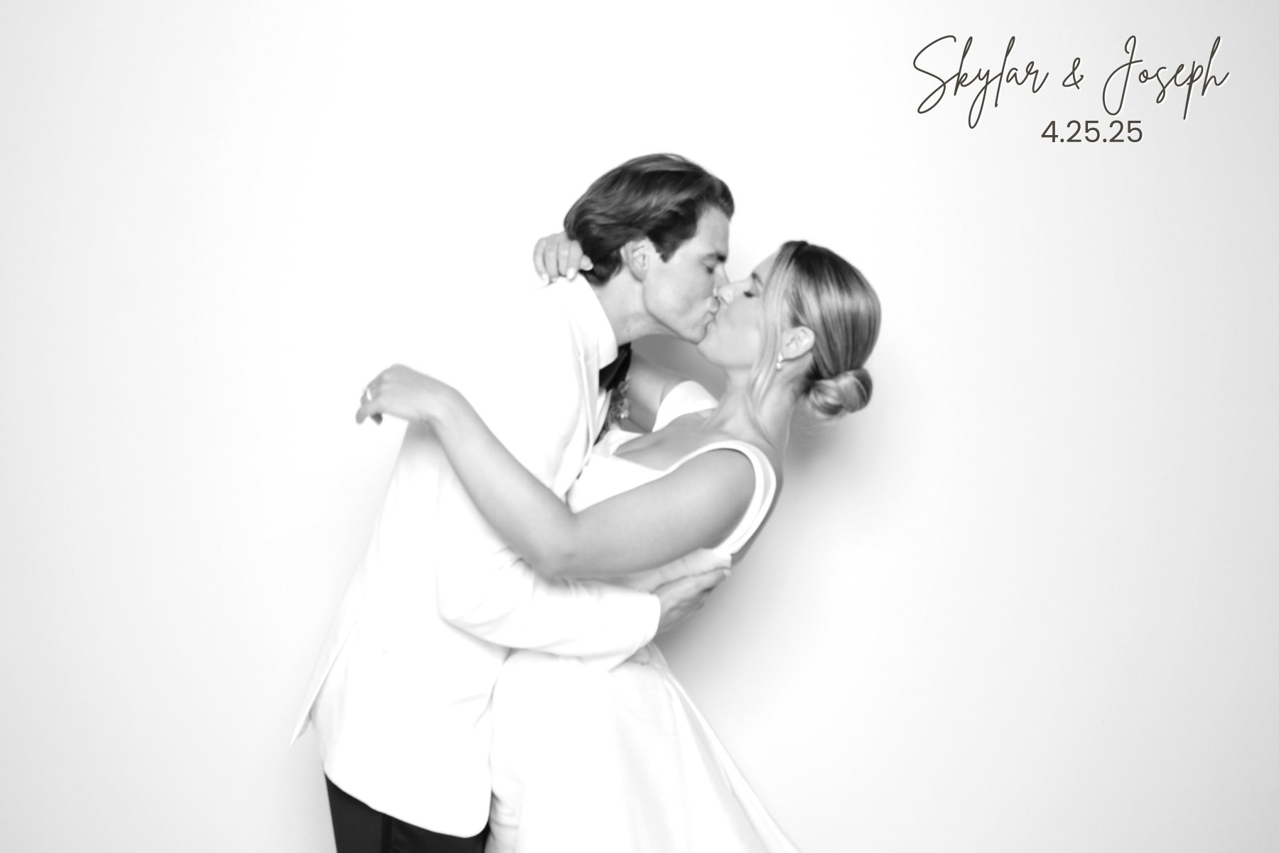 Couple in wedding attire shares a kiss against a bright studio backdrop.