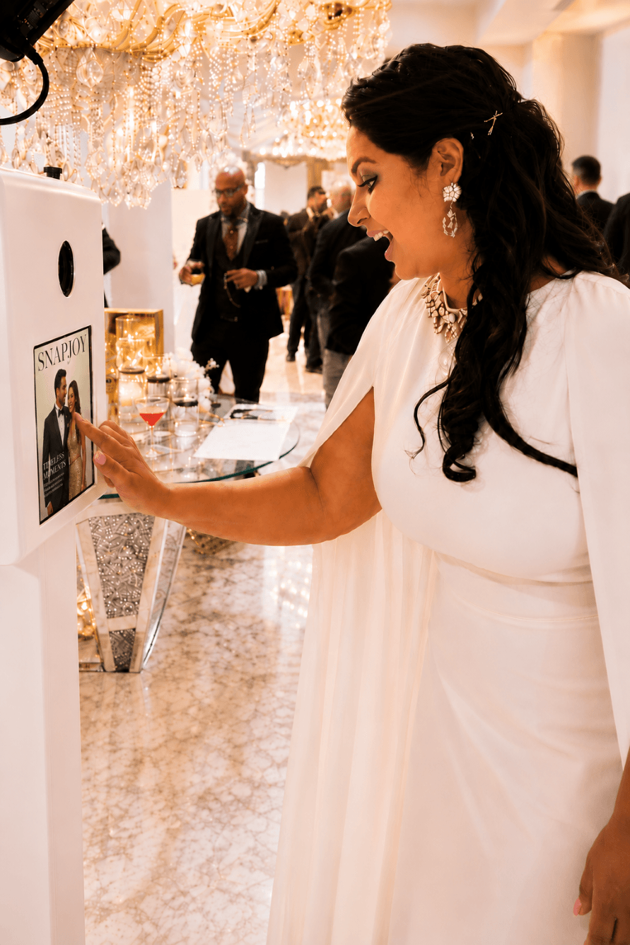 Elegant guest interacting with luxury photo booth touchscreen under chandeliers