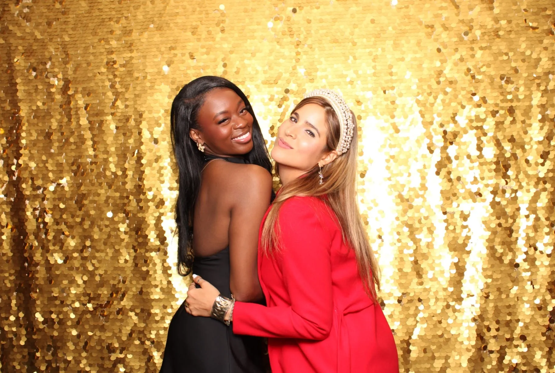 Two women in elegant attire on gold sequin wall