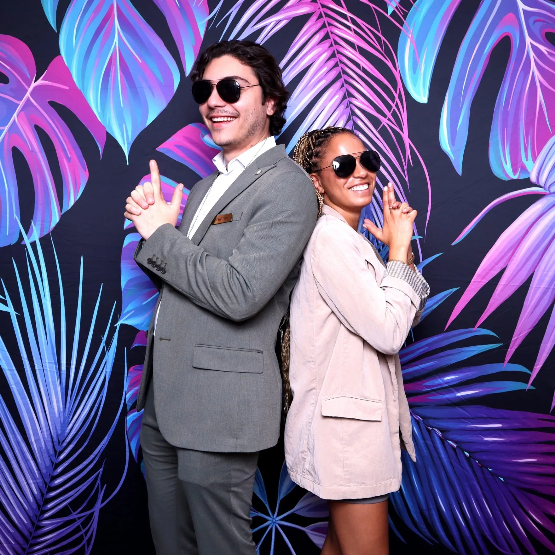 Couple posing back to back on neon palm backdrop