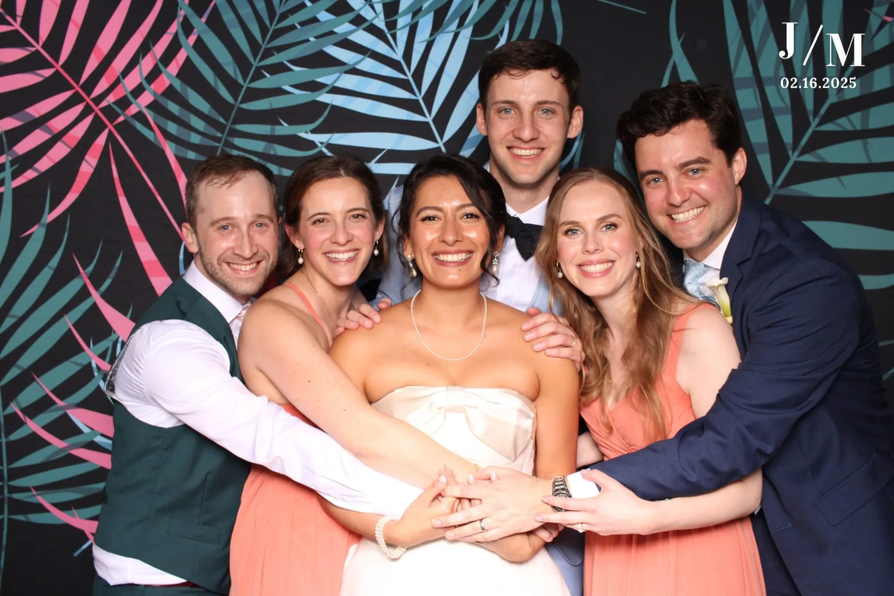 Wedding party group hug on teal and pink palm backdrop