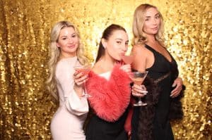 Elegant women enjoying drinks against a sparkling gold backdrop, capturing fun moments with SnapJoy Booth.
